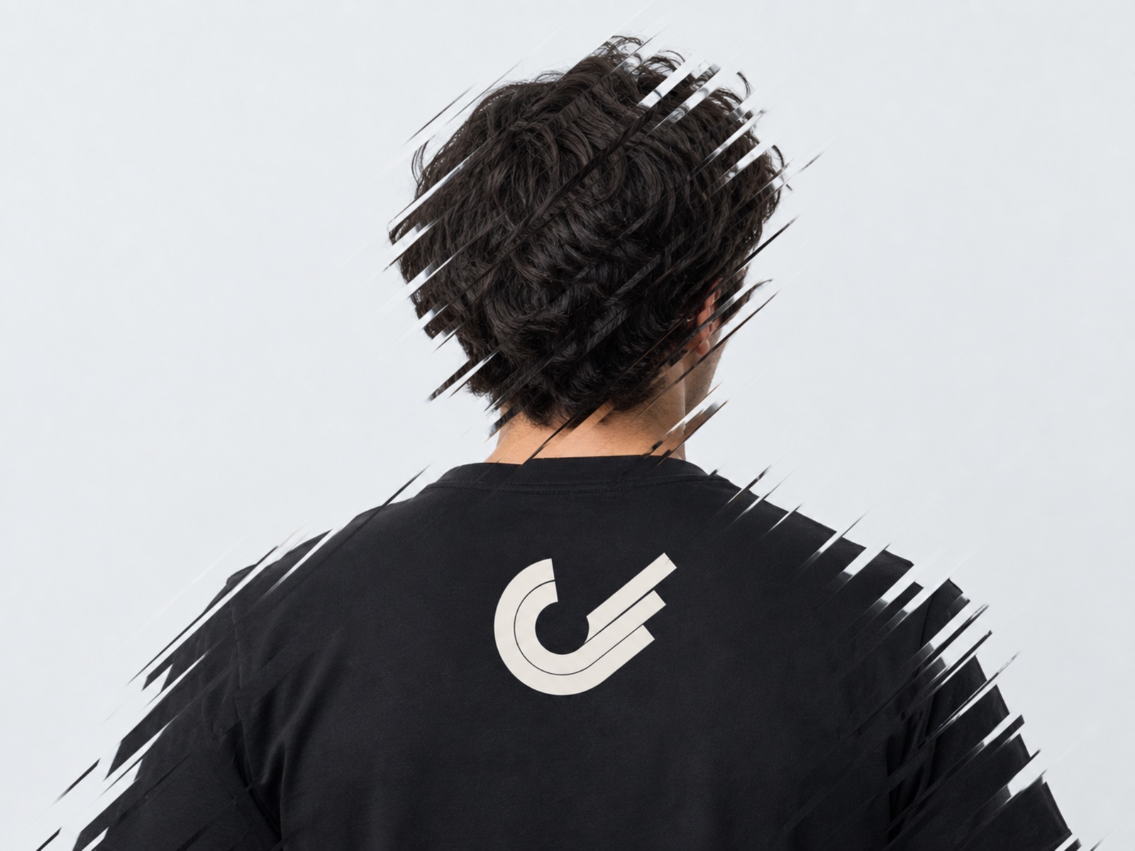 The one-color Slingshot mark between the shoulders of a black tee, with the photograph sliced along the mark's exit angle